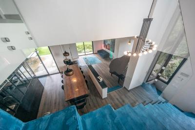 Jardin avec pelouse, arbre taillé, haies verdoyantes et maison moderne en arrière-plan sous un ciel partiellement nuageux.