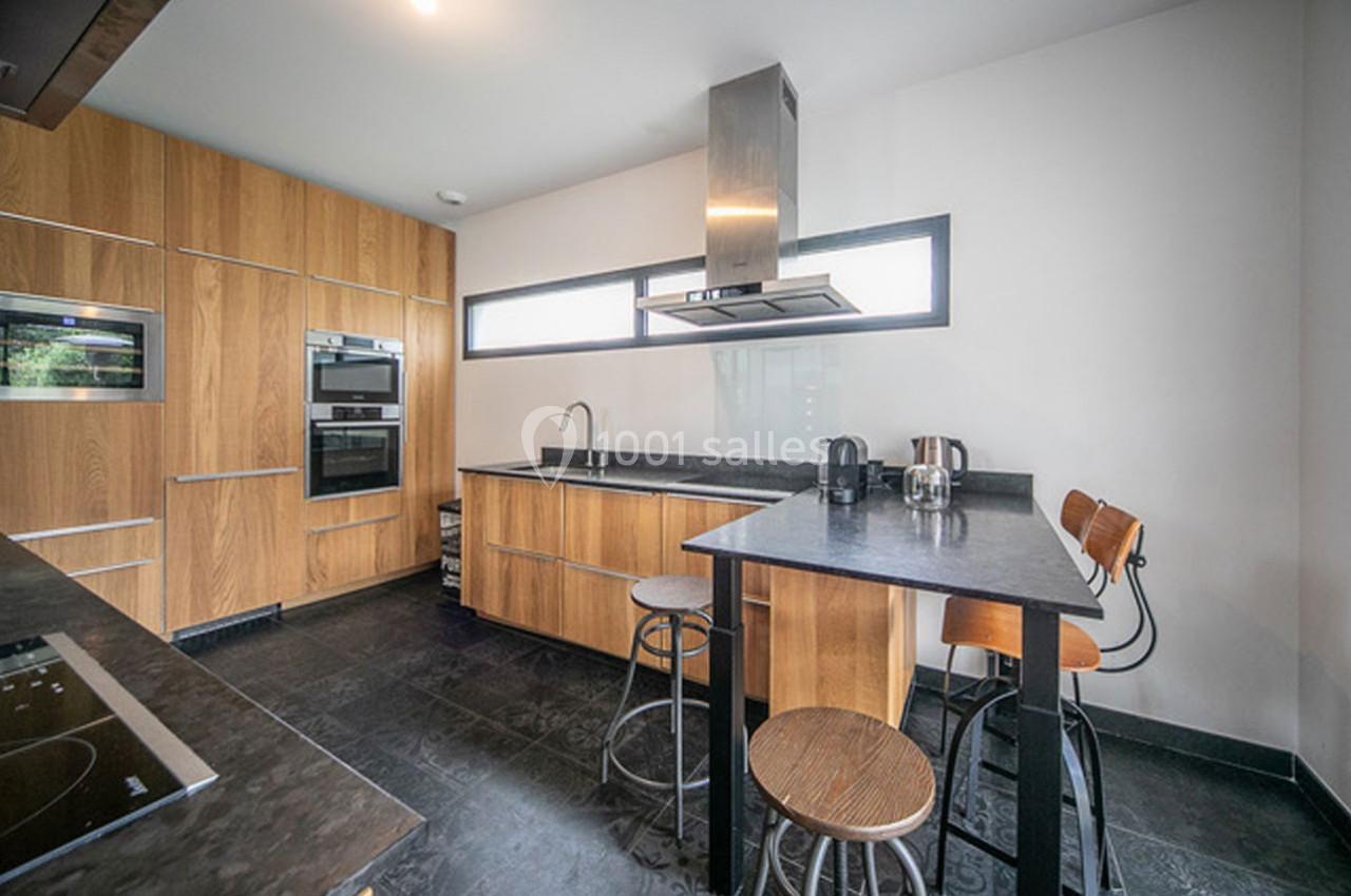 Cuisine moderne avec meubles en bois, plan de travail noir, îlot central avec tabourets et hotte en acier inoxydable.