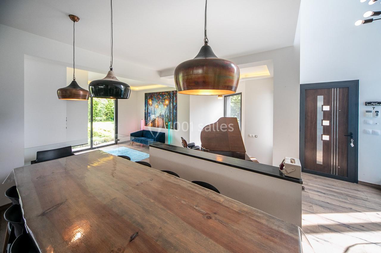 Salle à manger moderne avec table en bois, luminaires suspendus, piano et vue sur un jardin par une baie vitrée.