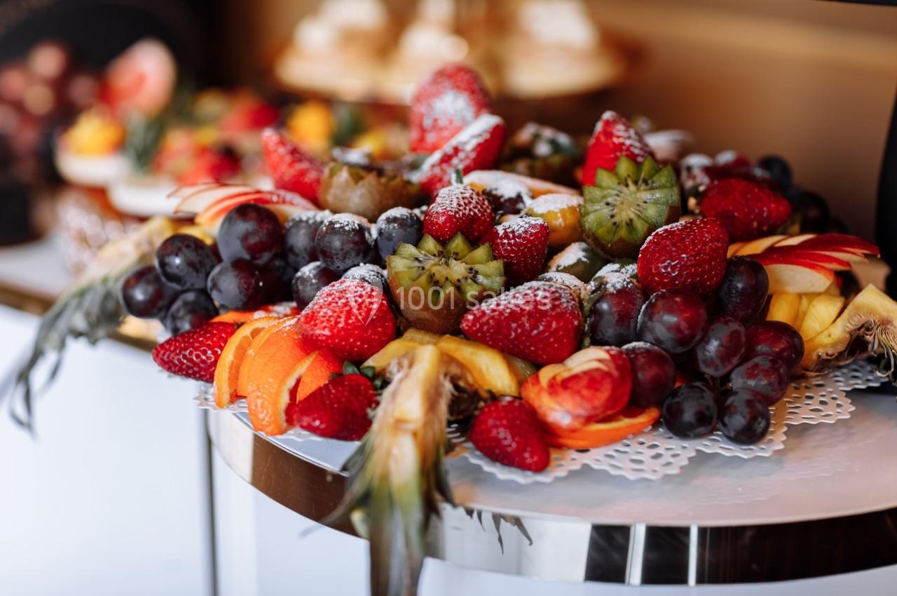 Plateau de fruits variés comprenant fraises, raisins, kiwis, tranches d'orange et pommes, présenté sur une table.