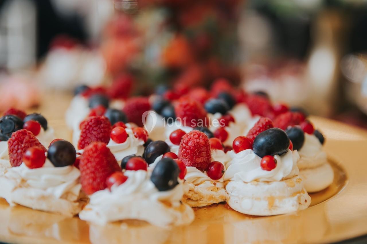 Petites meringues garnies de crème fouettée, framboises, myrtilles et groseilles sur un plateau doré.