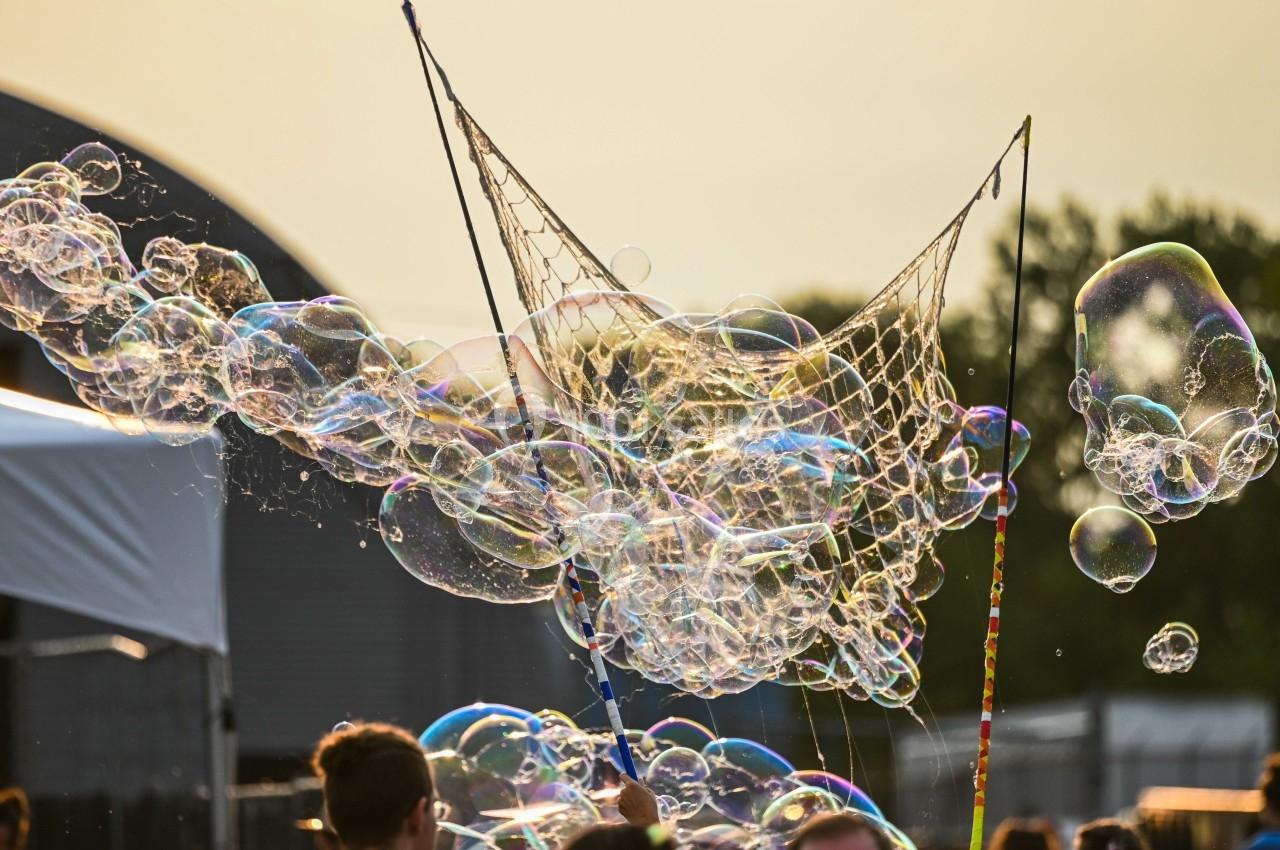 Bulles de savon colorées flottant dans l'air, créées avec un filet lors d'un événement en extérieur.
