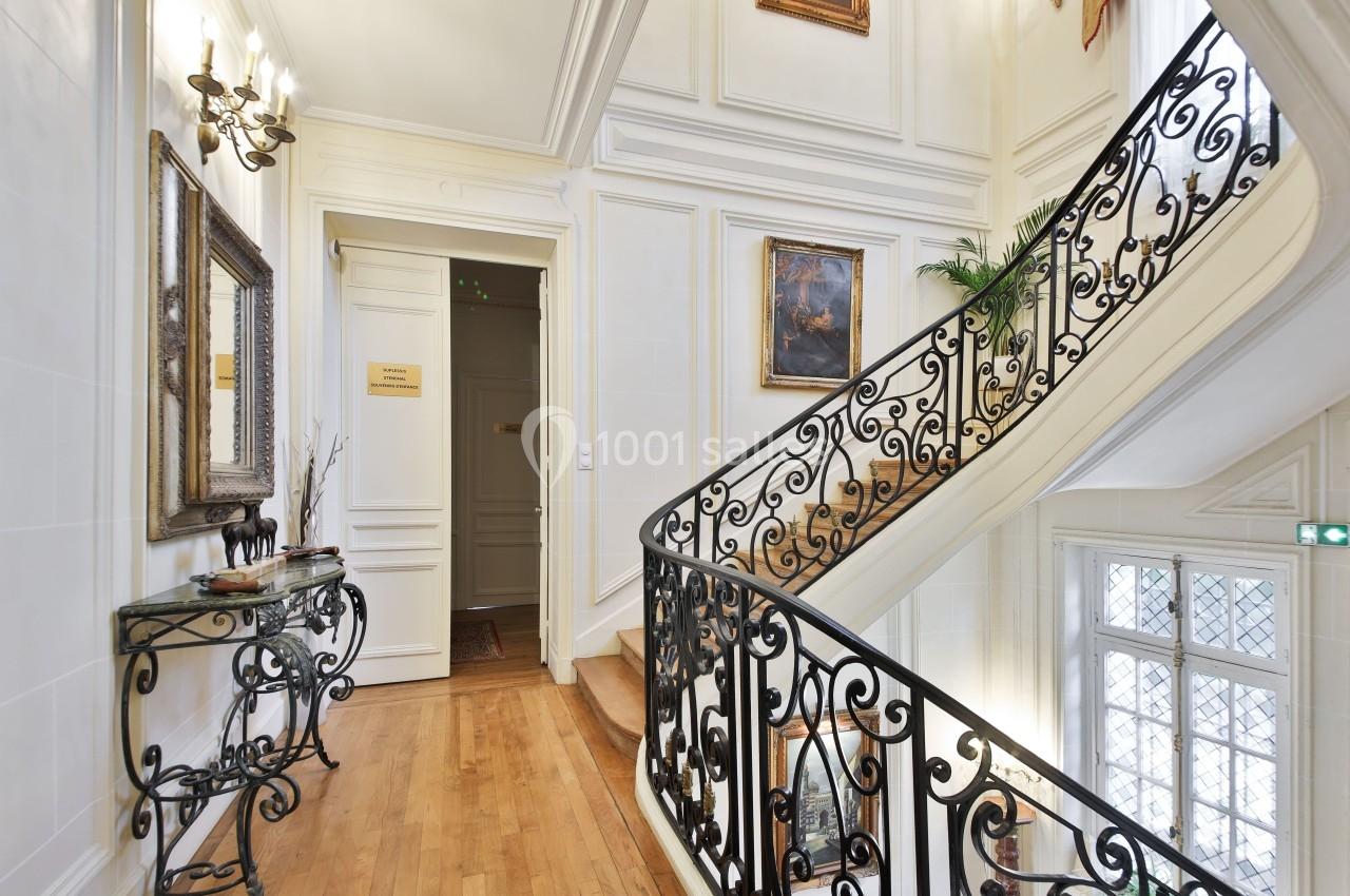 Escalier en colimaçon avec rampe en fer forgé, dans un intérieur lumineux avec parquet et décorations murales.