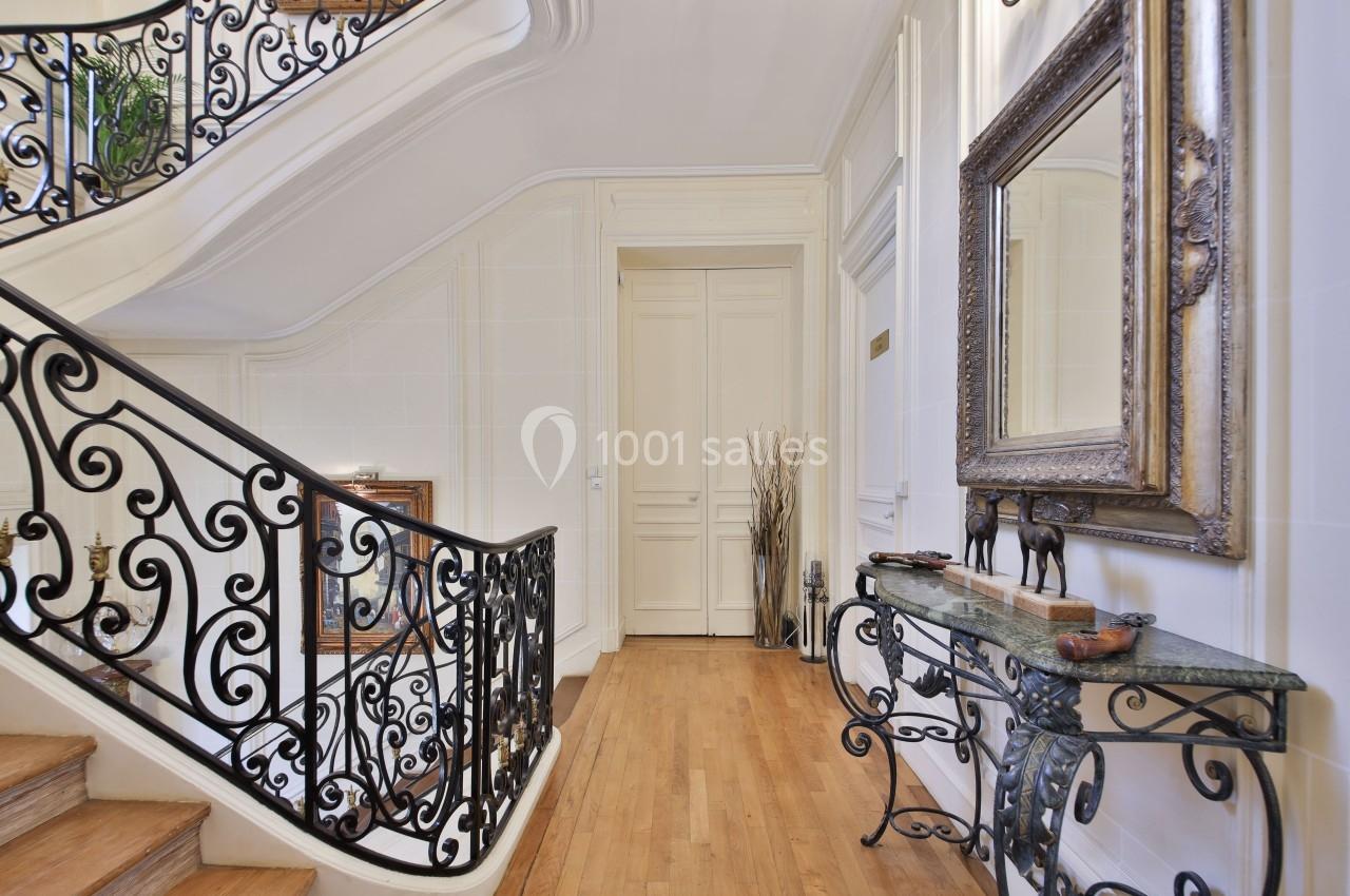 Escalier intérieur en bois avec rampe en fer forgé, console décorative et miroir dans un hall lumineux.