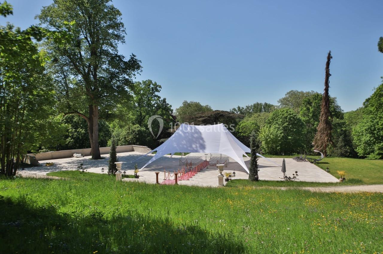 Tente blanche installée sur une terrasse en pierre entourée de verdure et d'arbres dans un cadre naturel.