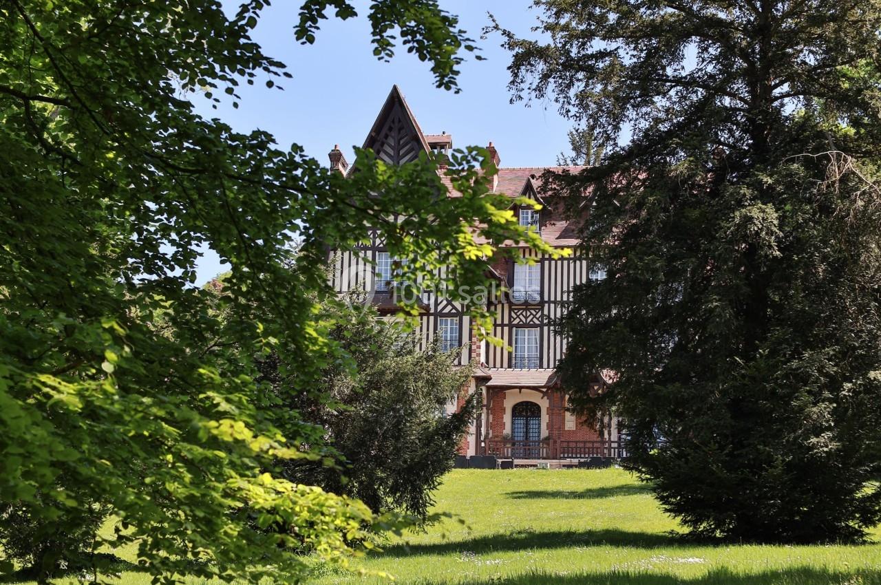 Manoir à colombages entouré d'arbres et d'une pelouse verdoyante sous un ciel bleu.