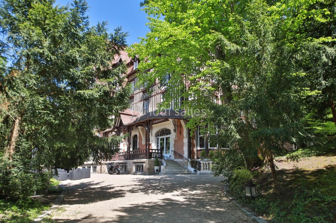 Façade d'une grande maison à colombages entourée d'arbres, avec une allée gravillonnée menant à l'entrée.