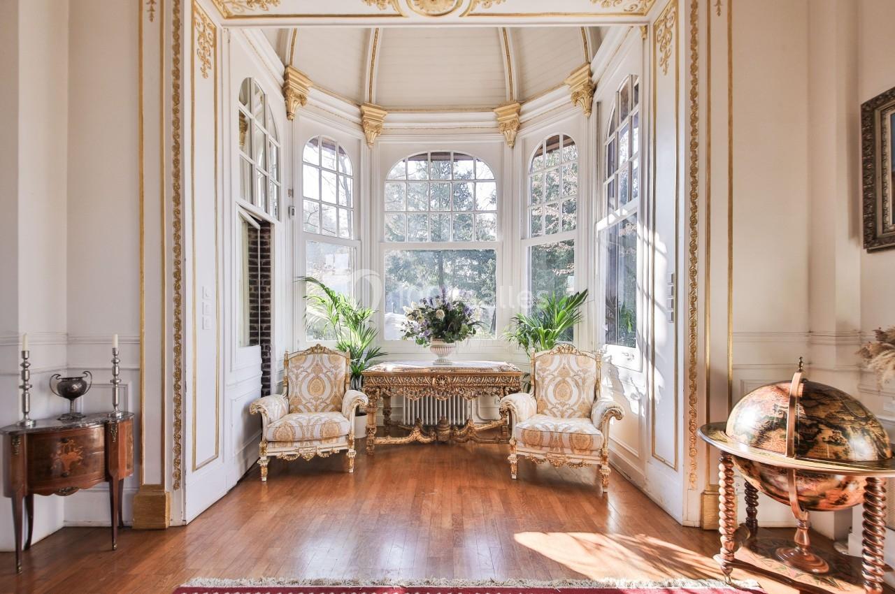 Salon lumineux avec grandes fenêtres cintrées, mobilier classique doré, globe terrestre et plantes décoratives.