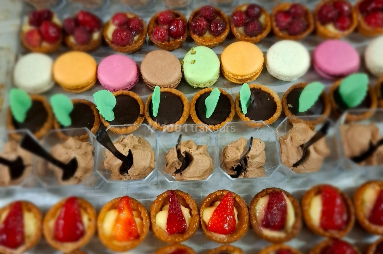 Plateau de desserts variés comprenant macarons, tartelettes aux fruits, chocolats et mousses présentés en rangées.