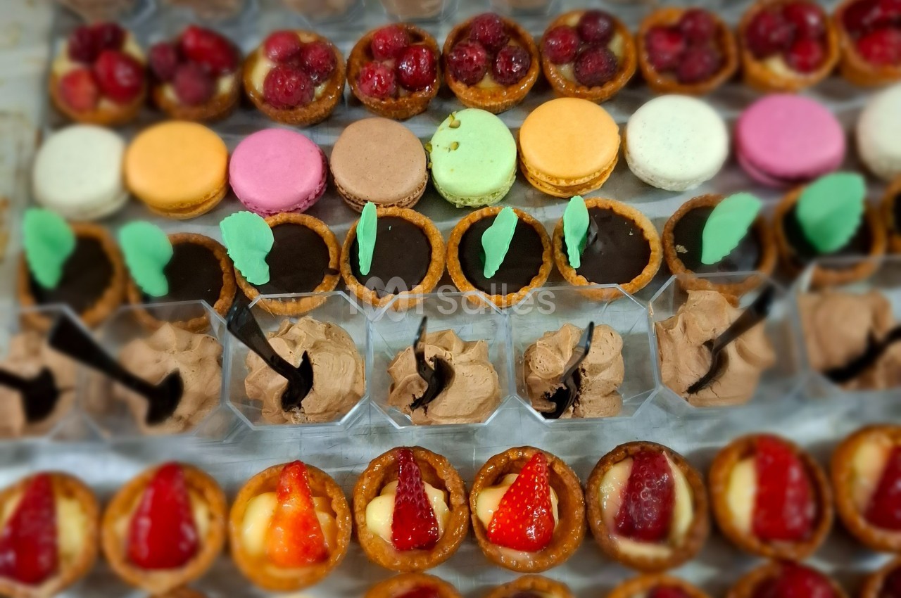 Plateau de desserts variés comprenant macarons, tartelettes aux fruits, chocolats et mousses présentés en rangées.