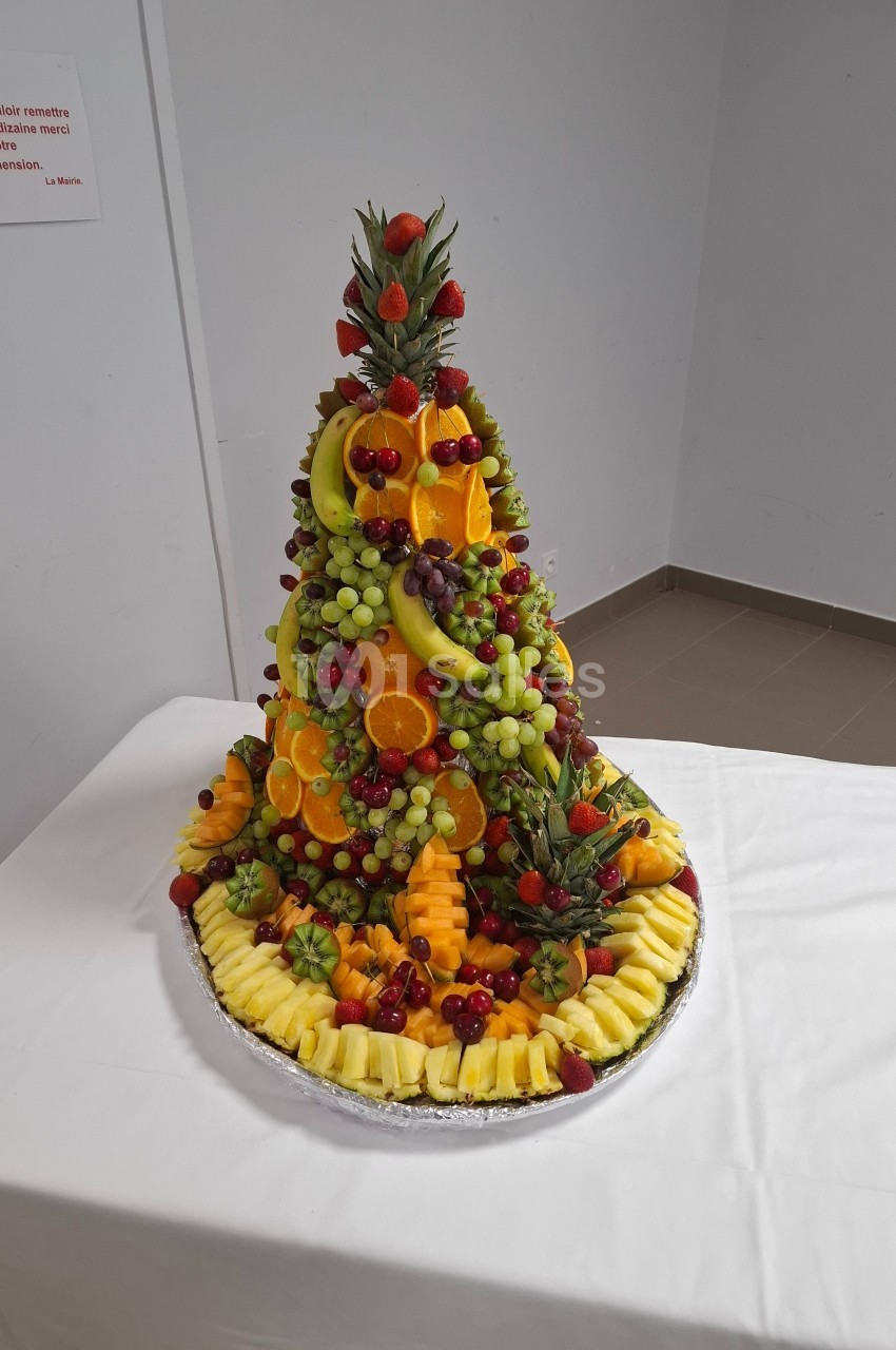 Plateau de fruits frais disposés en pyramide avec ananas, raisins, oranges, fraises et autres fruits colorés.