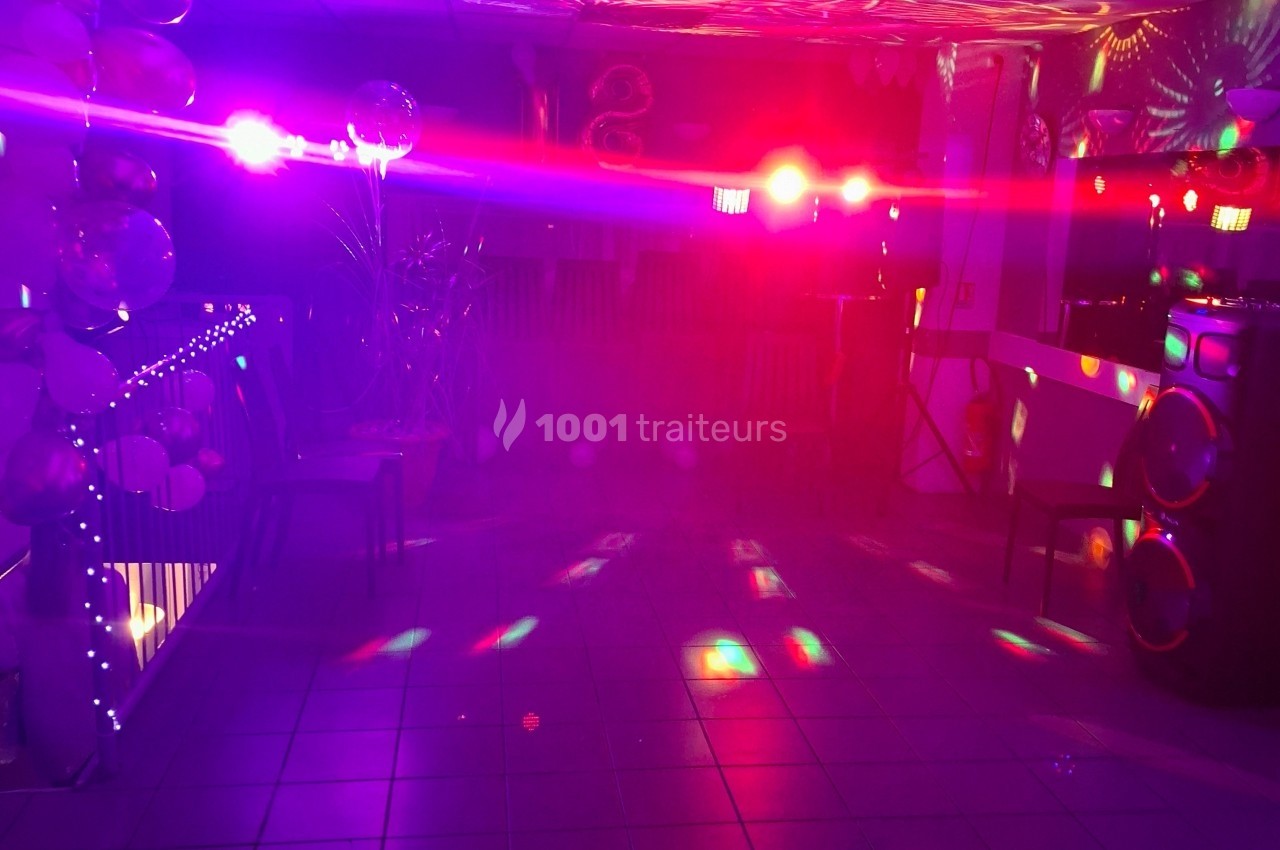 Salle éclairée par des lumières colorées et des projecteurs, avec des ballons et une ambiance festive.