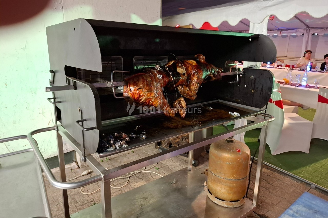 Un cochon entier rôti à la broche dans un four rotatif, avec des tables dressées en arrière-plan.