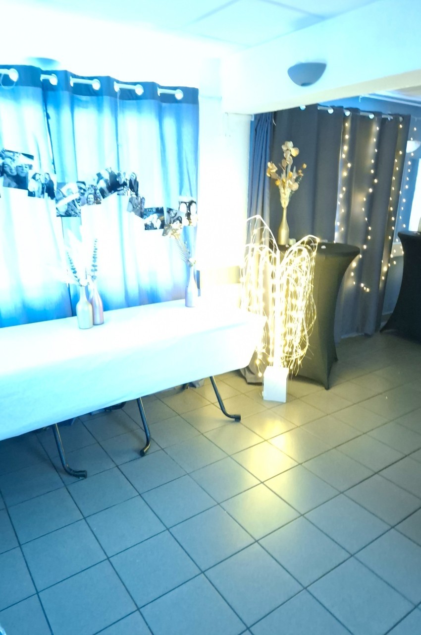 Salle décorée avec des rideaux bleus, guirlandes lumineuses, vases avec branches et une table recouverte d'une nappe blanche.