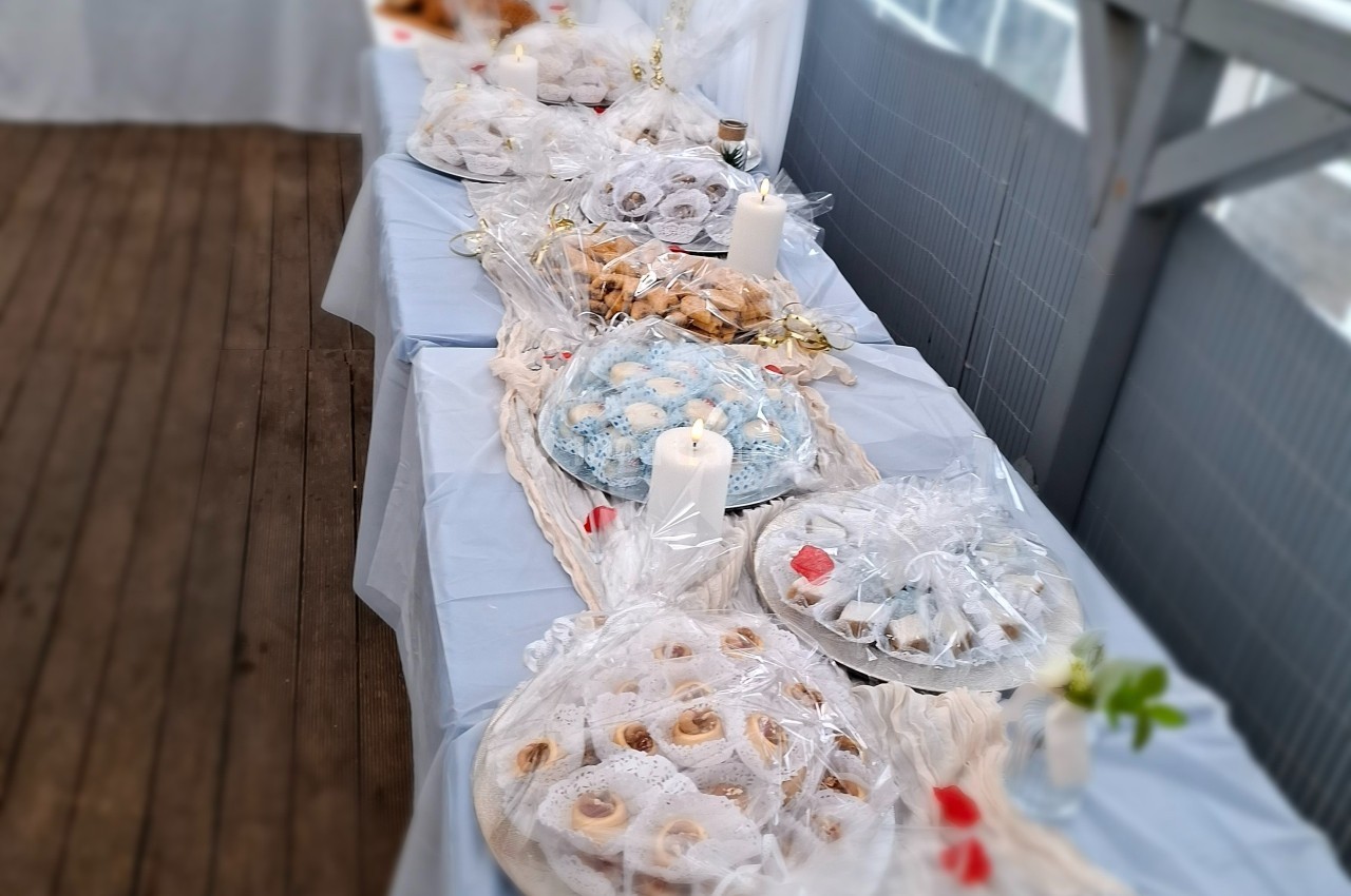 Table garnie de pâtisseries emballées dans du plastique transparent, décorée de bougies blanches et d'une nappe claire.