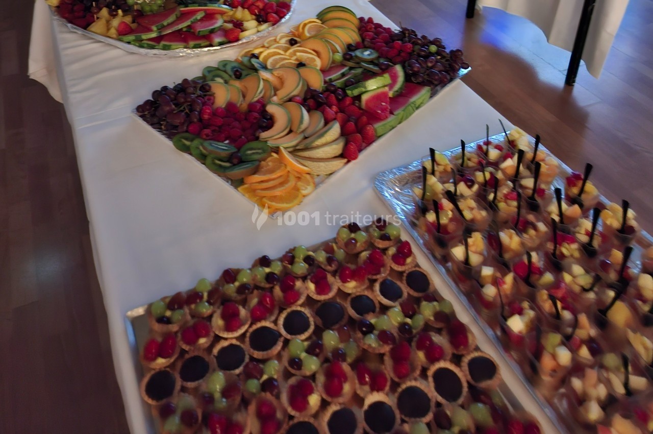 Plateaux de fruits frais découpés et assortiments de desserts variés disposés sur une table blanche.