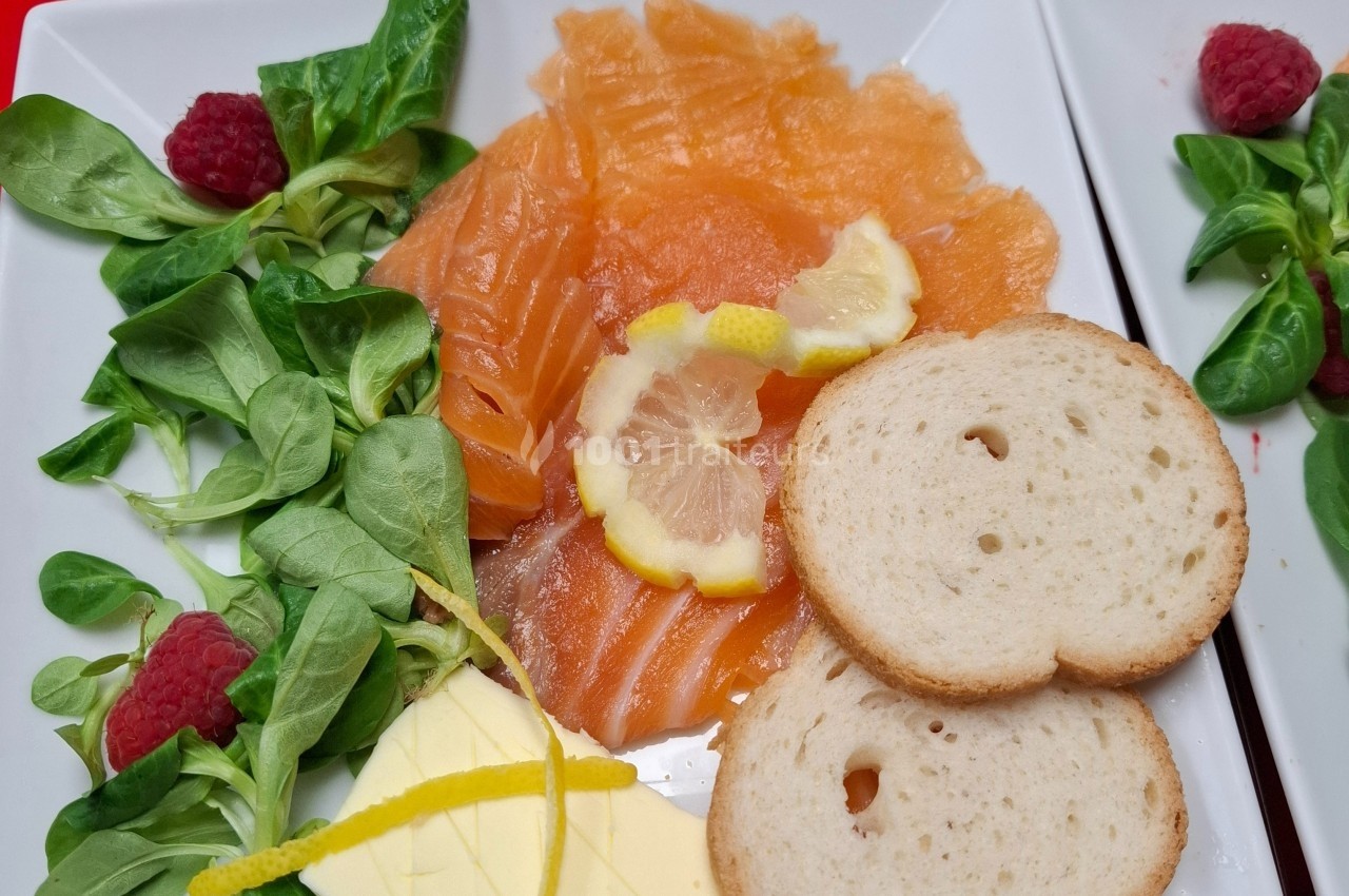 Assiette de saumon fumé avec rondelles de citron, mâche, framboises, tranches de pain et beurre.