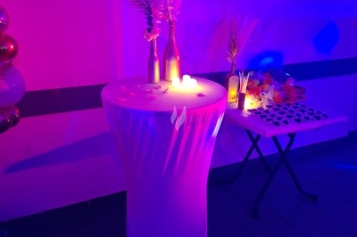 Salle décorée avec rideaux bleus, guirlandes lumineuses, vases avec fleurs et table recouverte d'une nappe blanche.