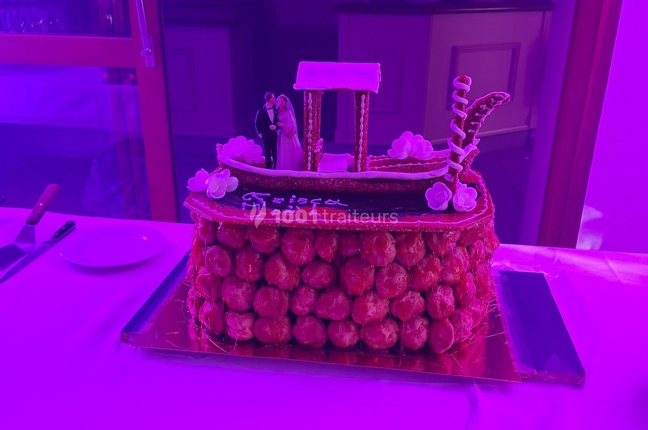 Pièce montée en choux décorée d'une gondole en sucre avec des figurines de mariés, éclairée par une lumière violette.