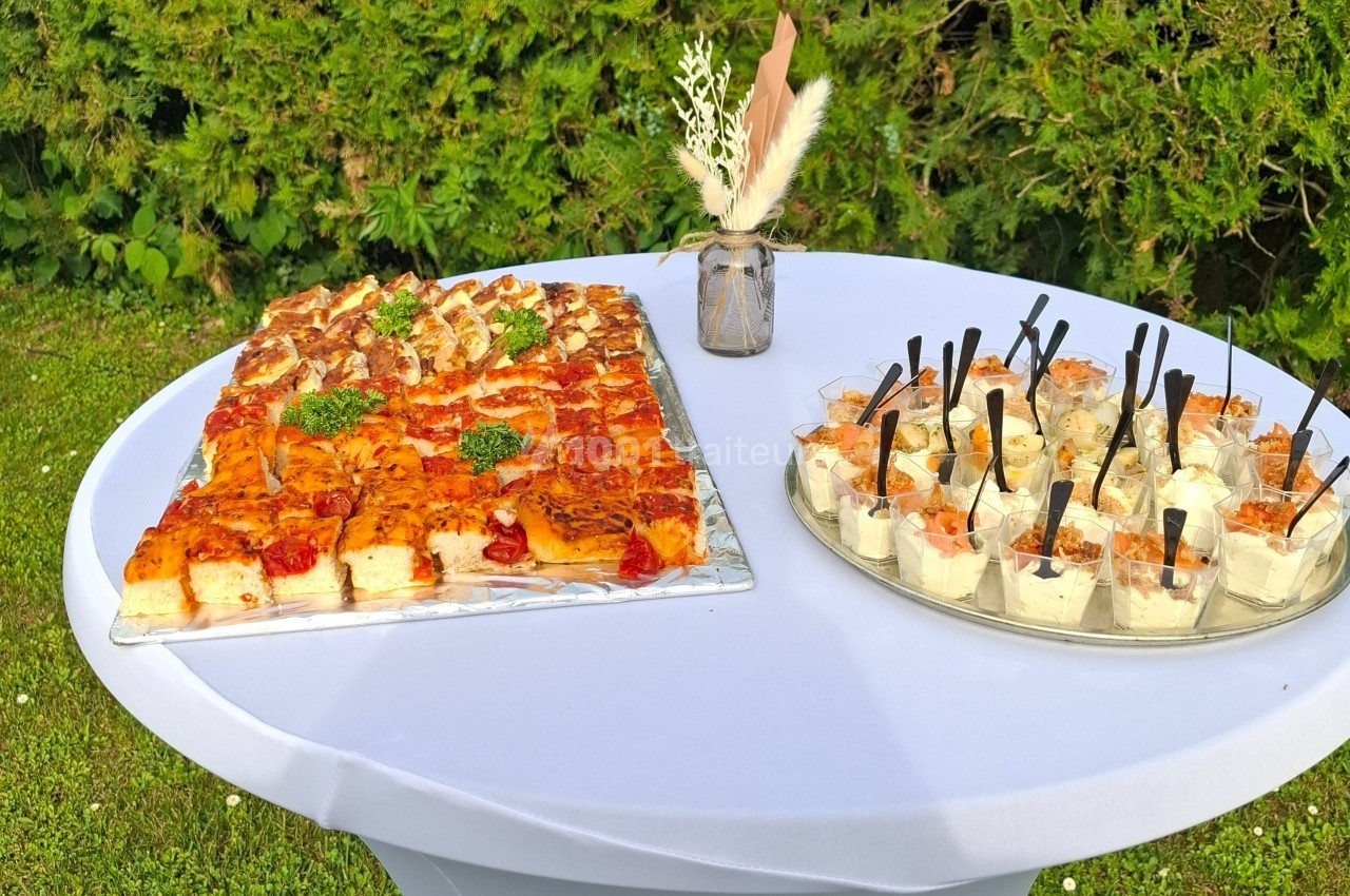 Plateau de bouchées salées et verrines disposé sur une table blanche en extérieur, avec un vase décoratif.