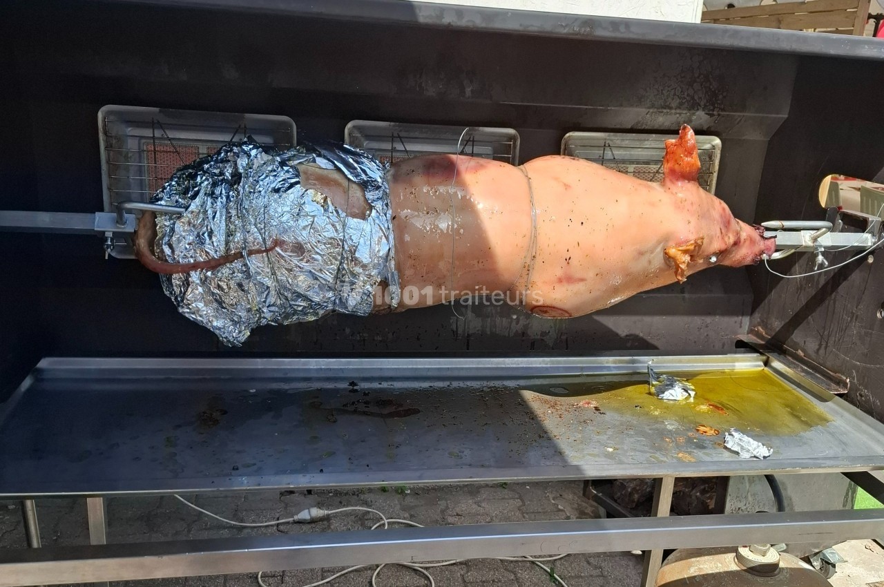 Cochon entier rôti à la broche dans un barbecue, partiellement recouvert de papier aluminium.