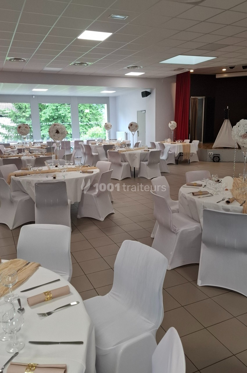 Salle de réception décorée avec des tables rondes, nappes blanches, chaises houssées et centres de table floraux.