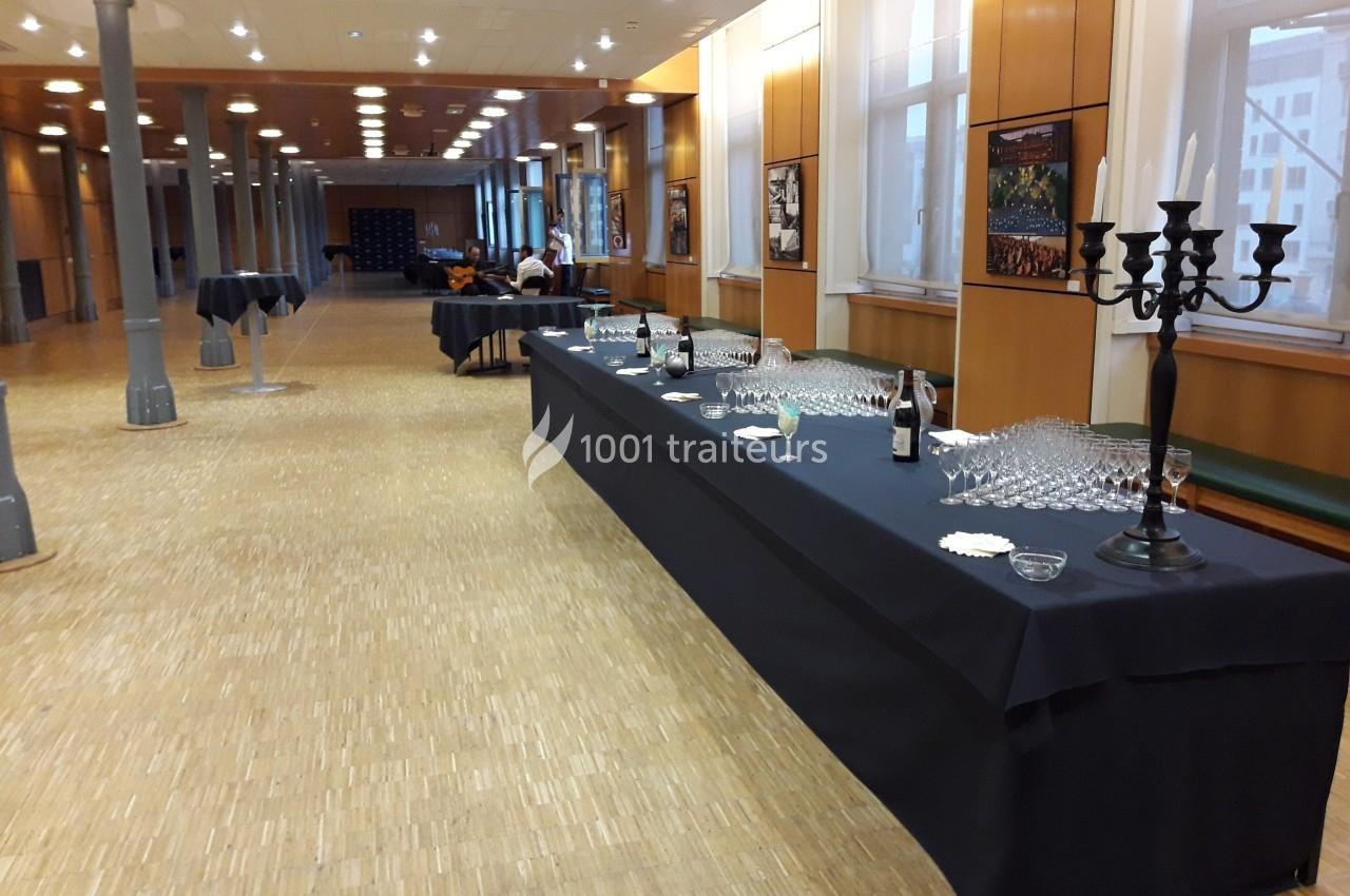 Salle de réception avec une table dressée pour un buffet, comprenant des verres, bouteilles et chandeliers noirs.