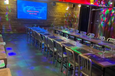Salle de restaurant avec longues tables dressées, éclairage tamisé et effets lumineux colorés sur le sol.