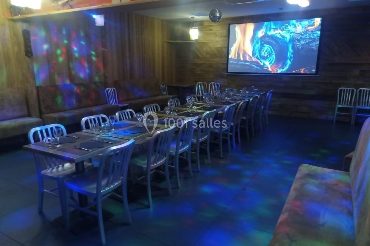 Salle de restaurant avec longues tables dressées, éclairage tamisé et projection d'une image sur un écran mural.