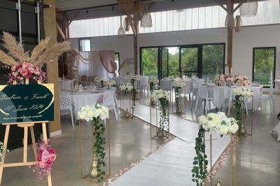 Centre de table floral avec roses blanches sur un support doré, dans une salle lumineuse avec grandes baies vitrées.