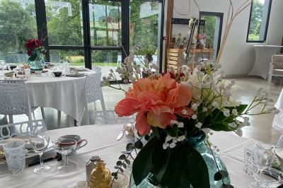Centre de table floral avec roses blanches sur un support doré, dans une salle lumineuse avec grandes baies vitrées.