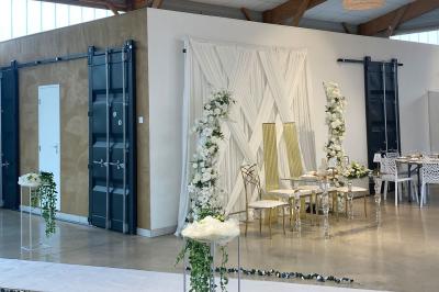 Centre de table floral avec roses blanches sur un support doré, dans une salle lumineuse avec grandes baies vitrées.