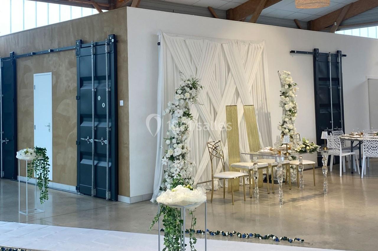 Salle décorée pour un événement avec une table élégante, des chaises dorées et des arrangements floraux blancs.