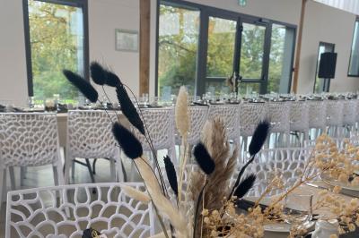 Centre de table floral avec roses blanches sur un support doré, dans une salle lumineuse avec grandes baies vitrées.