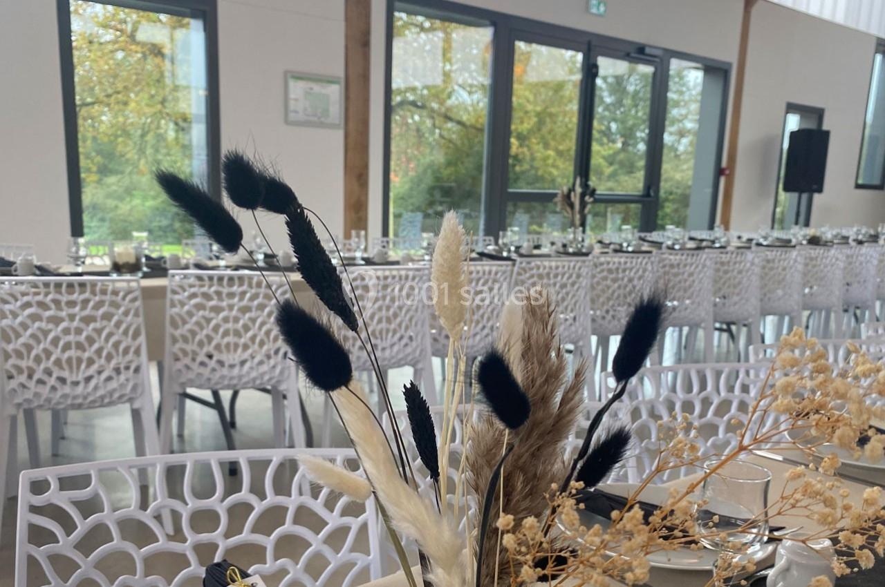 Salle de réception lumineuse avec tables dressées et décoration florale en herbes séchées au premier plan.