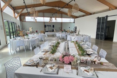 Centre de table floral avec roses blanches sur un support doré, dans une salle lumineuse avec grandes baies vitrées.