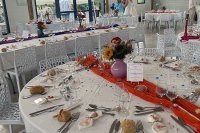 Centre de table floral avec roses blanches sur un support doré, dans une salle lumineuse avec grandes baies vitrées.