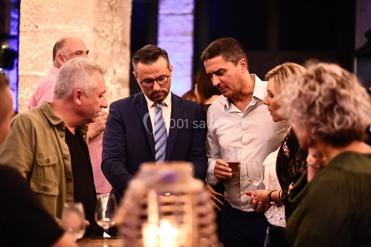 Un groupe de personnes échange autour d'une table lors d'un événement en intérieur, ambiance conviviale.