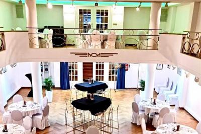 Salle de réception lumineuse avec tables rondes dressées, chaises blanches et éclairage violet au plafond.