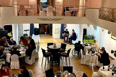 Salle de réception lumineuse avec tables rondes dressées, chaises blanches et éclairage violet au plafond.