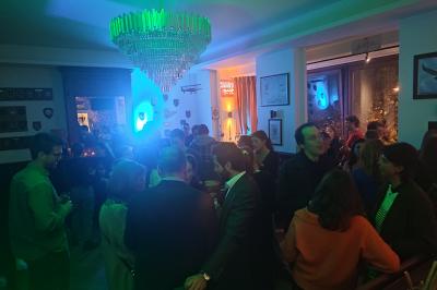 Salle de réception lumineuse avec tables rondes dressées, chaises blanches et éclairage violet au plafond.