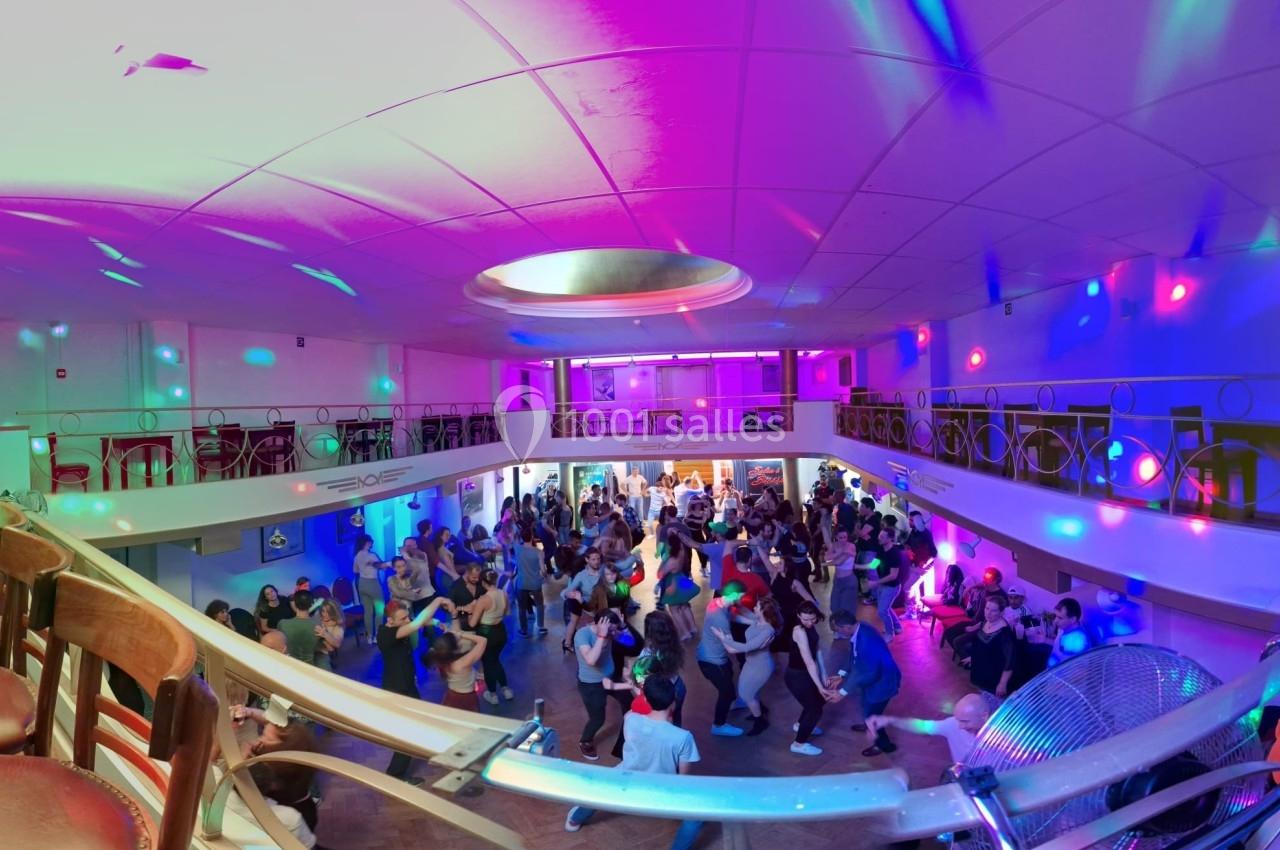Salle de danse animée avec des participants dansant sous des lumières colorées et un éclairage central circulaire.