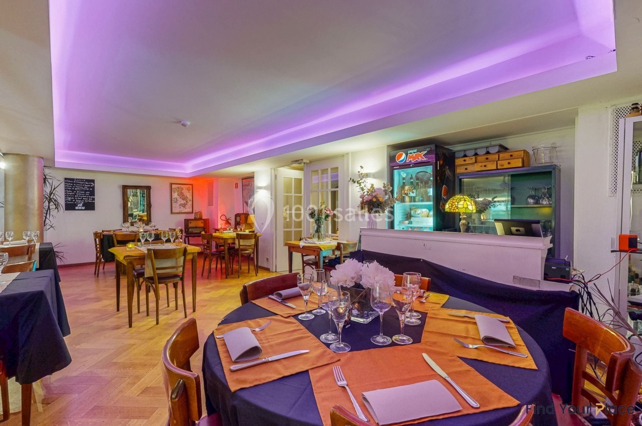 Salle de restaurant chaleureuse avec tables dressées, éclairage violet au plafond et décoration sobre.