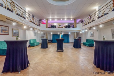 Intérieur d'un café lumineux avec canapés colorés, grandes fenêtres donnant sur une rue et un bar en arrière-plan.