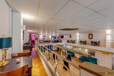 Intérieur d'un café lumineux avec canapés colorés, grandes fenêtres donnant sur une rue et un bar en arrière-plan.