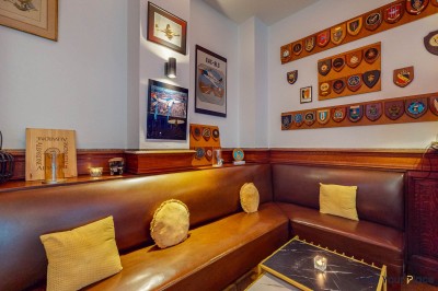 Intérieur d'un café lumineux avec canapés colorés, grandes fenêtres donnant sur une rue et un bar en arrière-plan.