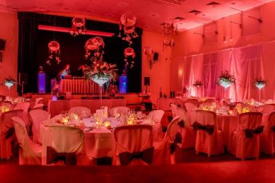 Salle de réception décorée avec des tables rondes, nappes blanches, éclairage rouge et arrangements floraux suspendus.