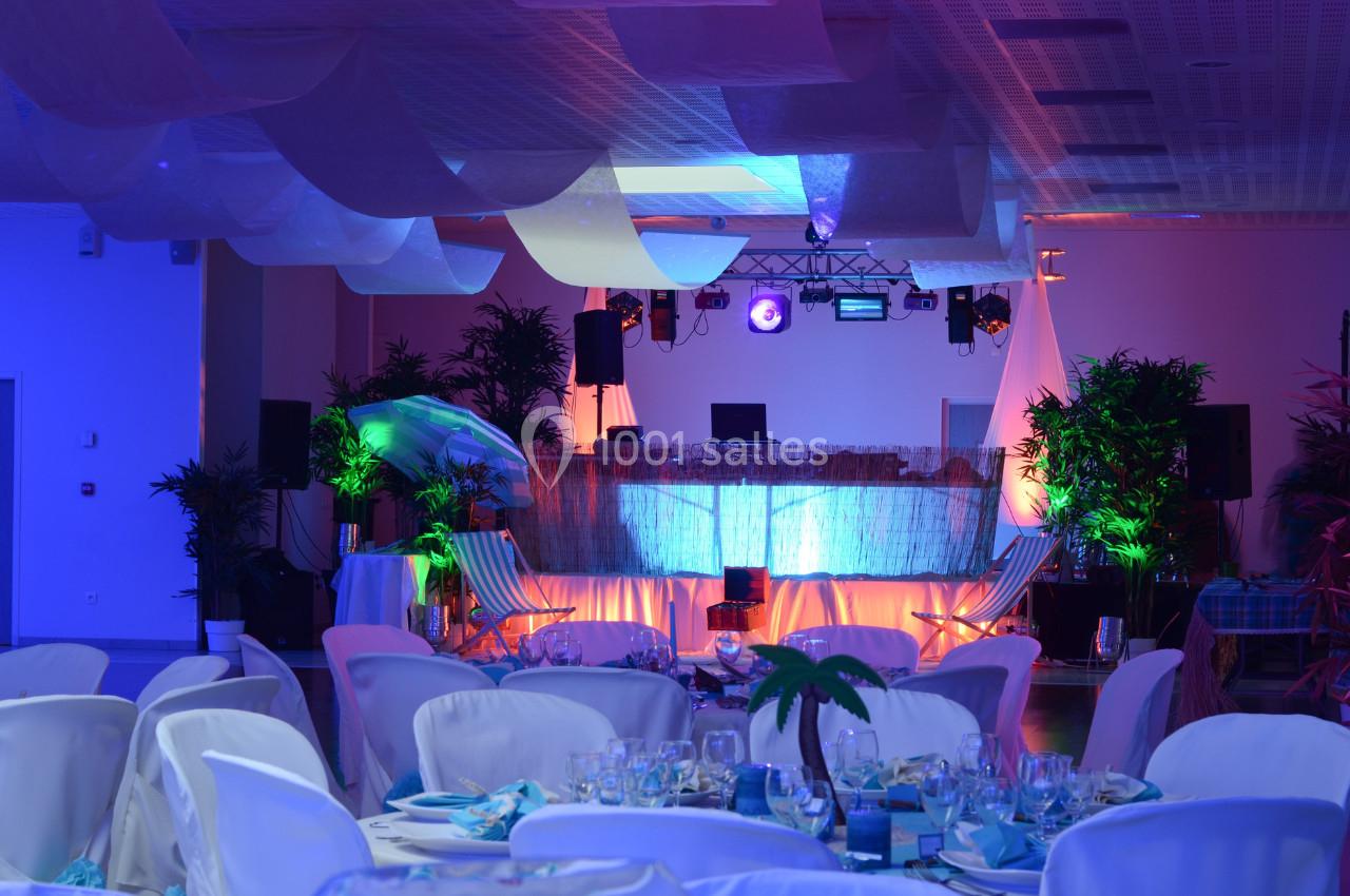 Salle de réception décorée avec des tables dressées, éclairages colorés et une scène équipée pour un DJ.