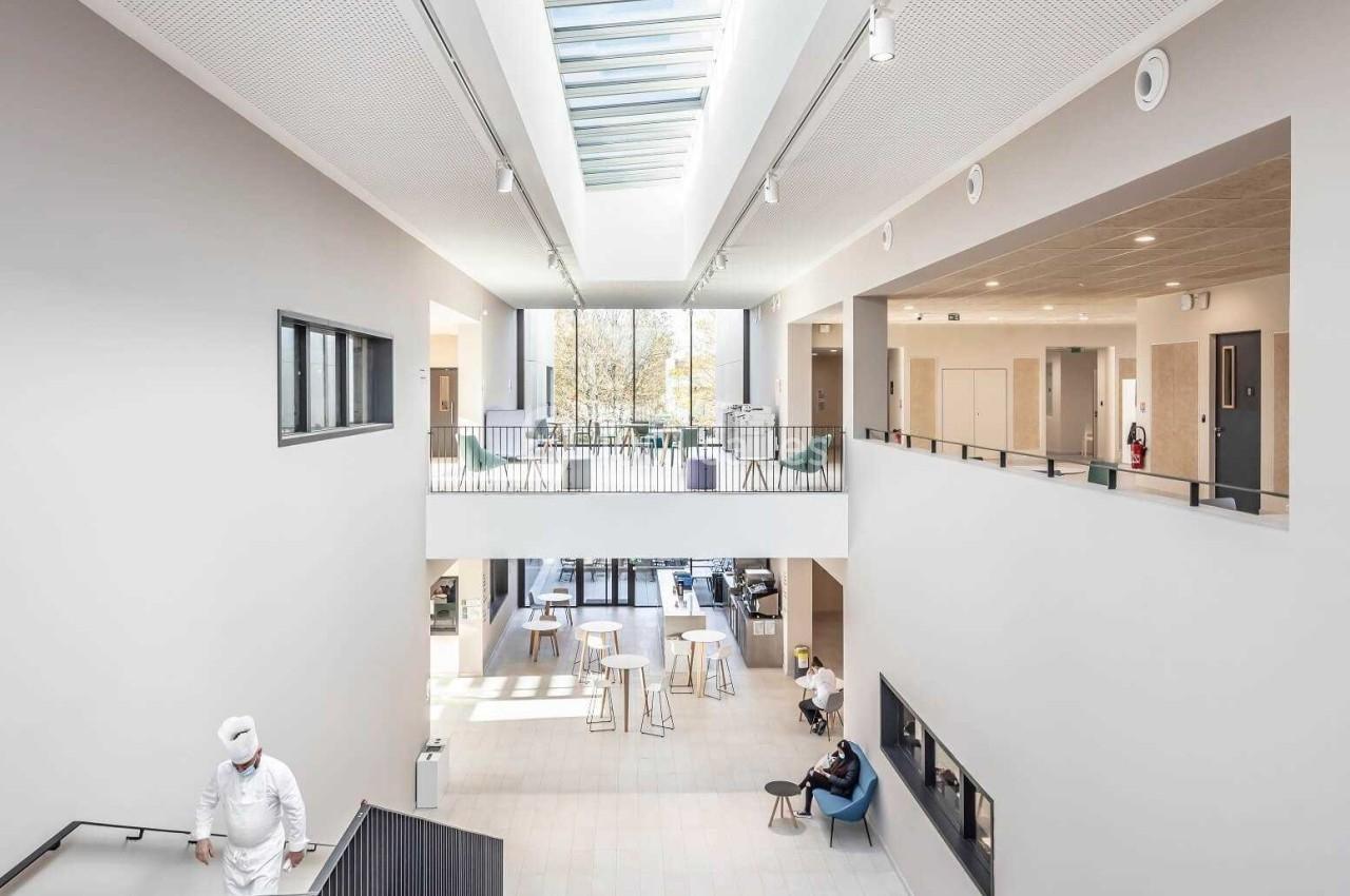 Vue intérieure d'un bâtiment moderne avec un grand atrium lumineux, des espaces ouverts et des personnes circulant.