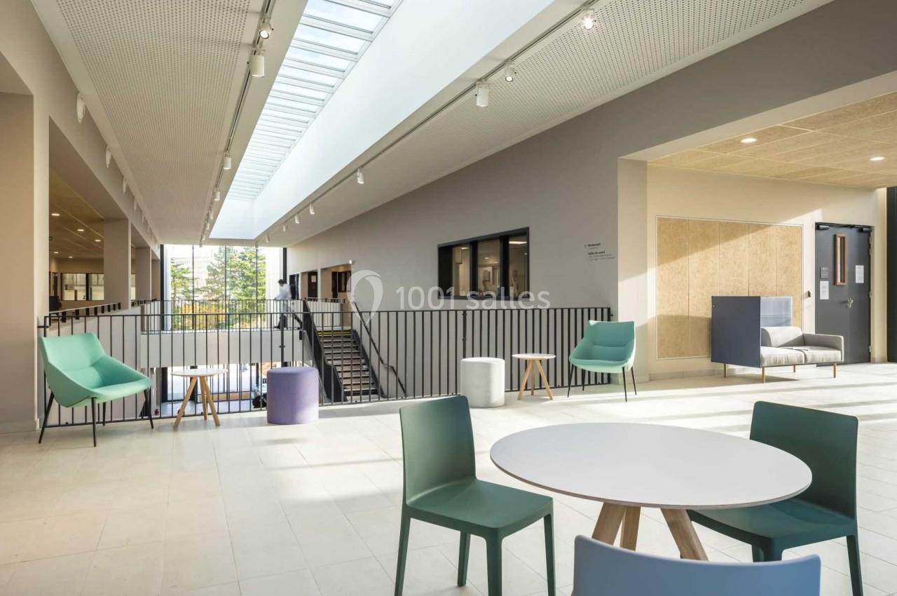 Espace lumineux avec mobilier moderne, tables et chaises colorées, situé près d'une rambarde et d'un escalier.